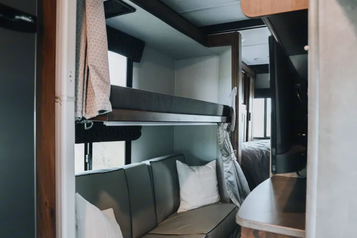 This RV rental interior features comfortable bunk beds over a sofa, with a glimpse of the main bedroom beyond.. Forester LE 2021