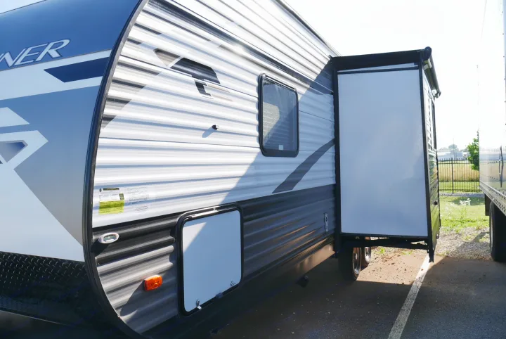 Side view of a modern RV rental, showing its extended slide-out and ribbed exterior, parked outdoors.. Heartland RVs Trailrunner 2021