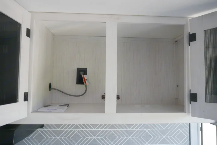Open white cabinet in an RV rental, featuring a power outlet and cable, providing convenient storage space.. Heartland RVs Trailrunner 2021