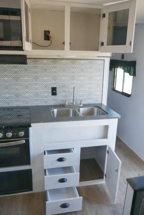 Modern RV kitchen setup with light cabinetry, sink, and appliances, ready for your next rv rental adventure.. Heartland RVs Trailrunner 2021
