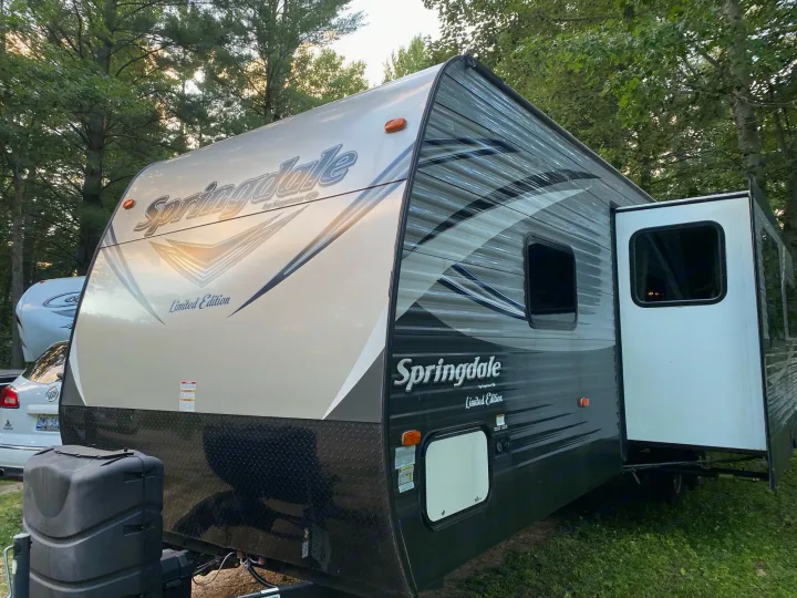 Front view of a Springdale travel trailer, ideal for rv rental, parked at a lush campsite with its slide-out extended.. keystone Springdale 2017