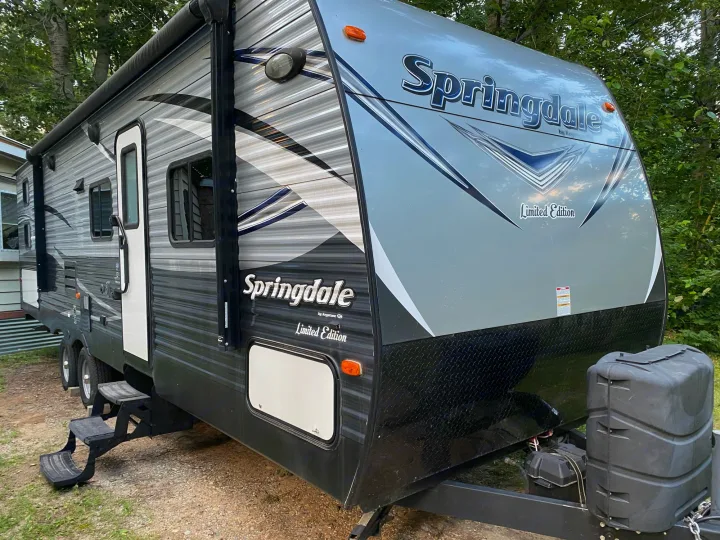 This grey & black Springdale travel trailer RV rental features an awning, steps, and front propane tanks.. keystone Springdale 2017