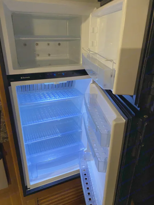 Dometic RV rental refrigerator and freezer interior, empty and clean with clear shelves and blue LED lighting.. keystone Springdale 2017