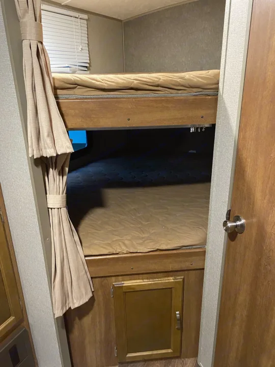 Interior of an **rv rental**: two stacked bunk beds with mattresses, tied-back curtains, and a lower storage cabinet.. keystone Springdale 2017