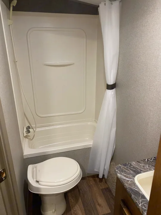Inside an RV rental: a compact bathroom featuring a shower/tub combo, toilet, and vanity sink.. keystone Springdale 2017