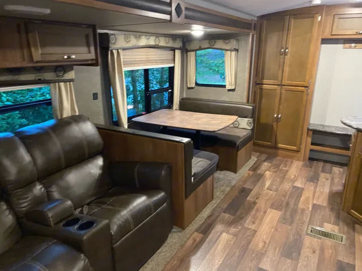 Inside an RV rental: comfortable brown reclining sofa, dining booth with table, and wood-look laminate flooring in the living area.. keystone Springdale 2017