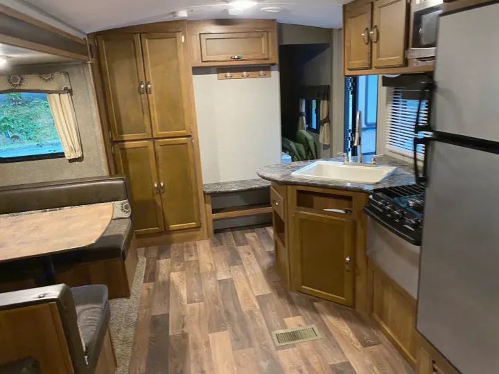 Inside a modern RV rental, featuring a full kitchen, comfortable dinette, and wood-look flooring.. keystone Springdale 2017