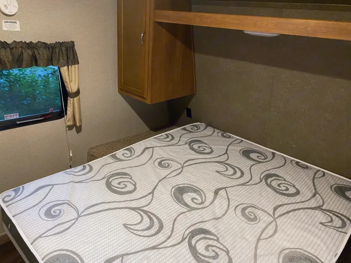 Inside an RV rental: a cozy bedroom with a patterned mattress, window view, and overhead storage.. keystone Springdale 2017