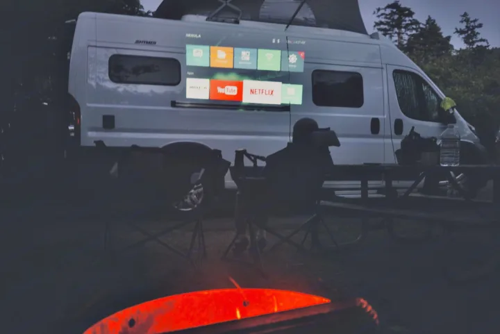 Enjoying an RV rental adventure: a camper watches Netflix projected on the van's side, beside a glowing fire.. Hymer Hymer Class B 2019