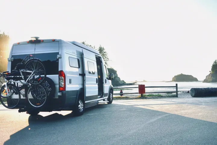 RV rental with bikes on back, parked by a sunny beach with ocean views. Perfect for coastal travel and adventure.. Hymer Hymer Class B 2019