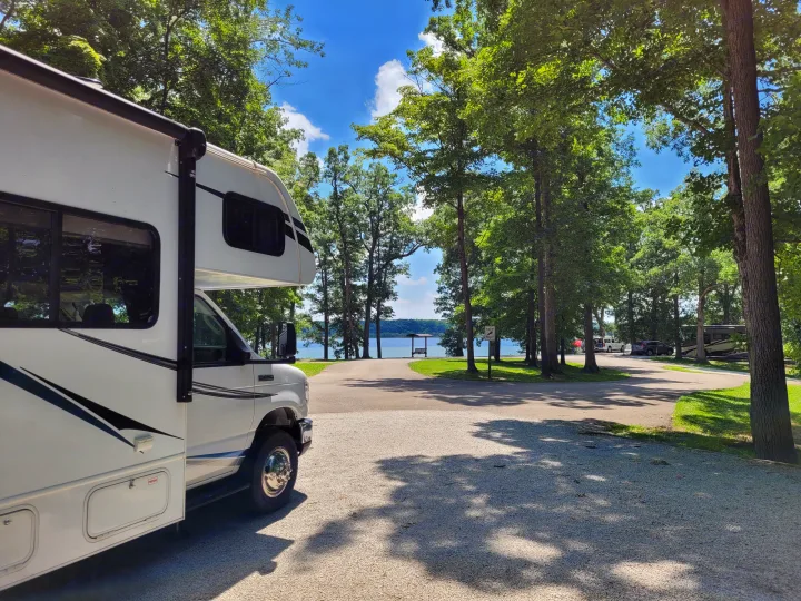 White RV rental parked at a sunny lakeside campground, showcasing serene waters, green trees, and blue skies.. Forest River Sunseeker LE 2018