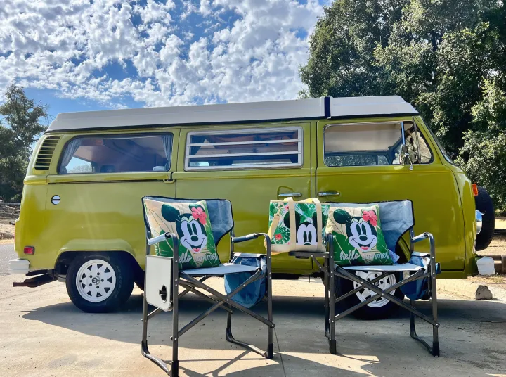 This vintage lime-green camper van, ideal for an RV rental, features Mickey Mouse summer pillows and chairs for outdoor relaxation.. Volkswagen Kombi T2 Westfalia 1976