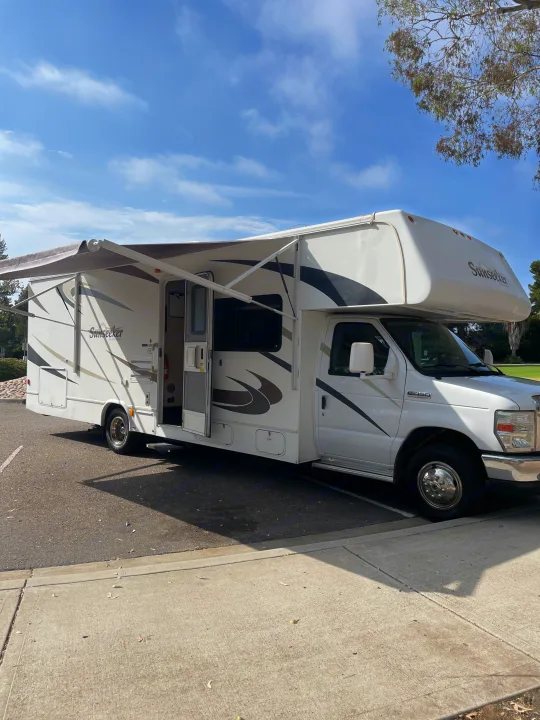 White Sunseeker RV rental with awning extended, parked on asphalt. Ready for camping and travel adventures.. Forest River Sunseeker 2009