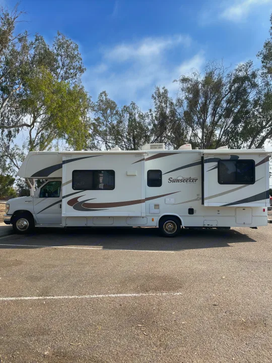 A white Sunseeker E450 Class C RV rental, ready for travel, parked on asphalt with trees under a blue sky.. Forest River Sunseeker 2009