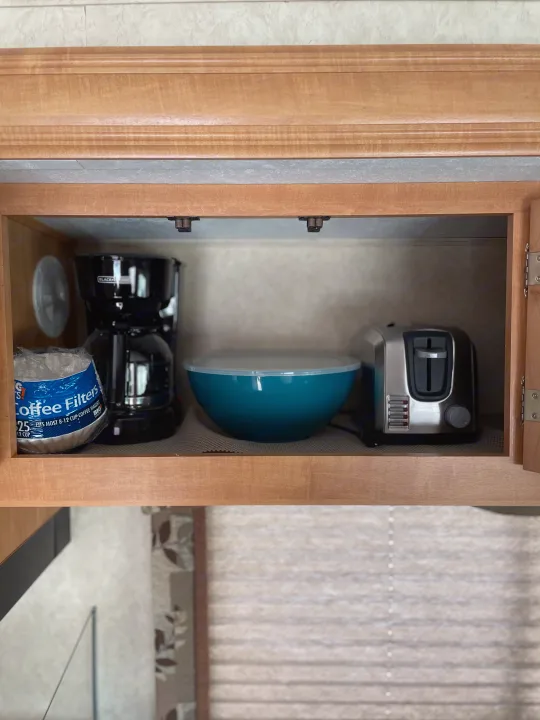 Compact RV rental kitchen cabinet neatly organized with a coffee maker, toaster, coffee filters, and a mixing bowl.. Forest River Sunseeker 2009