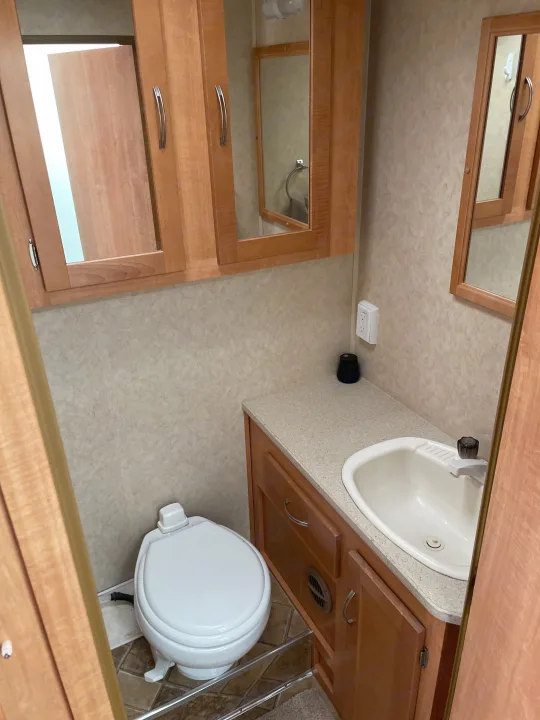 Compact bathroom in an RV rental, featuring a toilet, sink, and mirrored cabinets, designed for travel convenience.. Forest River Sunseeker 2009