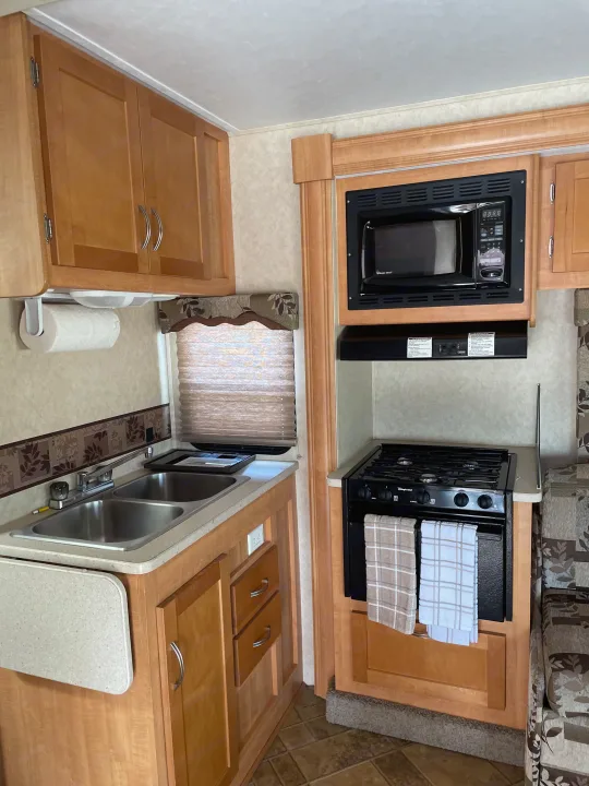 Spacious RV rental kitchen with microwave, stove, double sink, and ample cabinets, ideal for road trips.. Forest River Sunseeker 2009