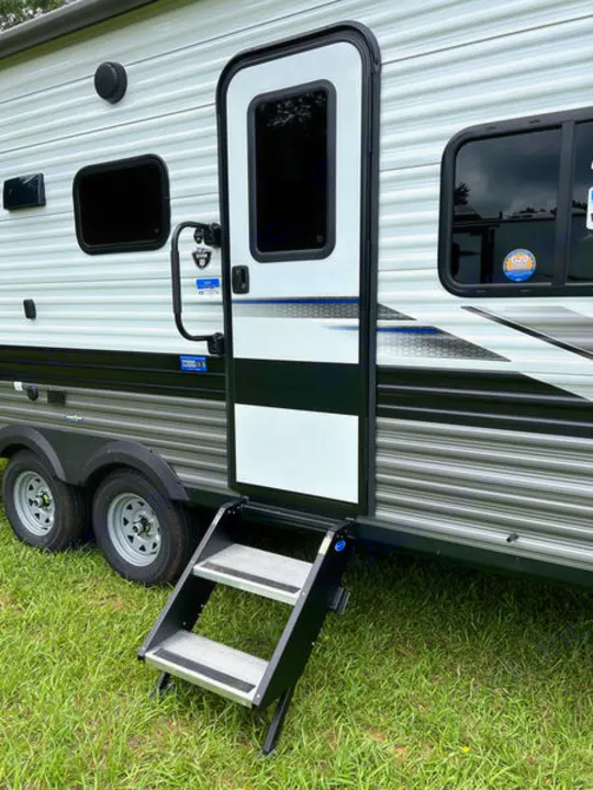 This RV rental shows the exterior of a white and grey travel trailer with its entry door open and steps extended, parked on green grass.. jayco Jay Flight 2022