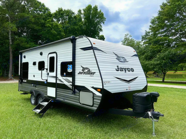 Spacious Jayco travel trailer RV rental, featuring white and gray design, parked on grass by a lake with trees.. jayco Jay Flight 2022