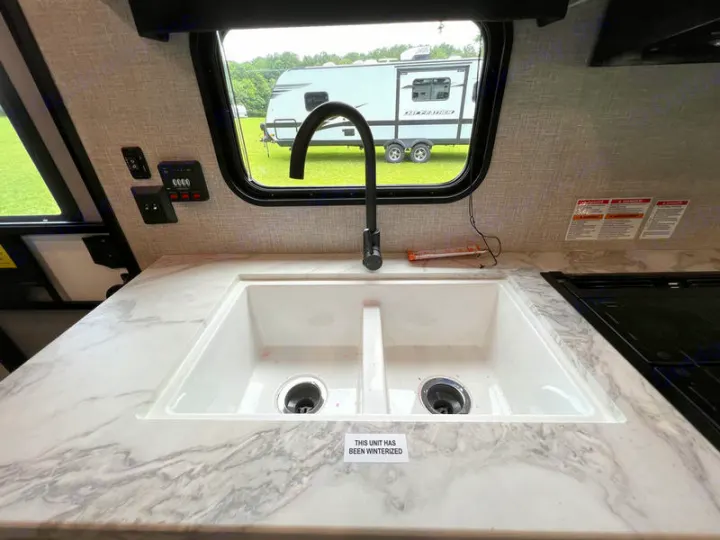 Inside an RV rental: kitchen sink, faucet, and counter with controls. "Unit winterized" sign visible on the sink.. jayco Jay Flight 2022