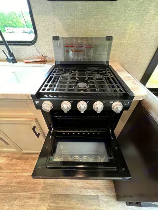 Inside an RV rental, a black gas range with four burners and the oven door open, showing the compact interior.. jayco Jay Flight 2022