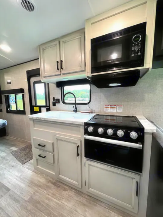 Modern RV rental kitchen featuring light cabinets, a microwave, stove, oven, and sink area. Light wood-look flooring.. jayco Jay Flight 2022