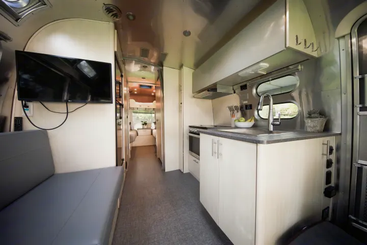 Inside this modern rv rental: sleek kitchen, lounge with TV, and a hallway to the cozy bedroom.. Airstream Flying Cloud 2021