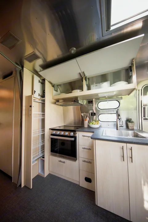 Modern RV rental kitchen interior with oven, sink, overhead storage, and pull-out pantry. Bright & functional.. Airstream Flying Cloud 2021