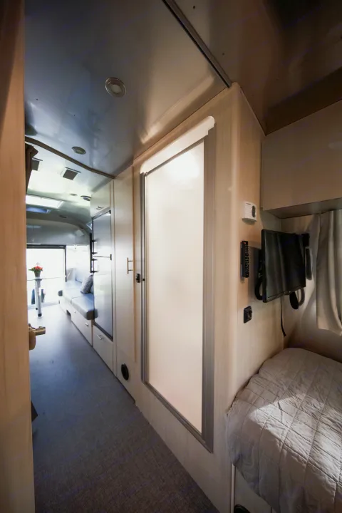 Step inside this modern RV rental! View of its compact interior with a bed, living space, and frosted glass shower.. Airstream Flying Cloud 2021