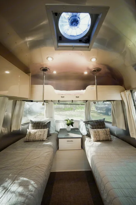 Spacious RV rental interior featuring cozy twin beds, an overhead bunk, and bright natural light. Ideal for a travel adventure.. Airstream Flying Cloud 2021