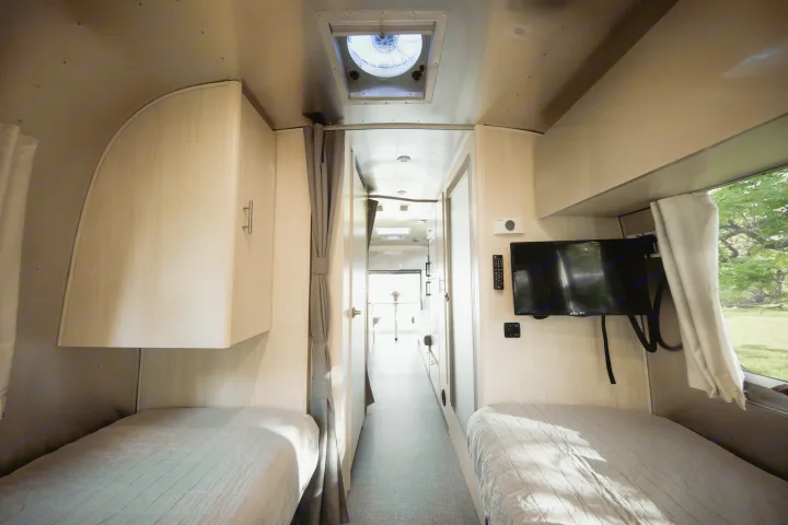 Inside a comfortable RV rental: Twin beds, overhead cabinets, TV, and a view of nature from this inviting camper interior.. Airstream Flying Cloud 2021