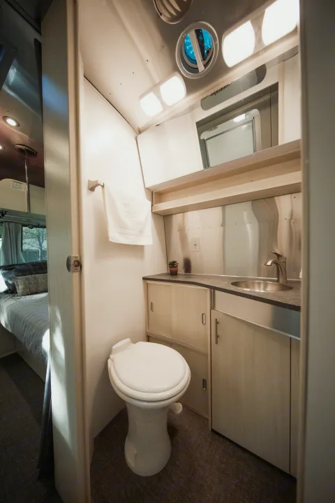 Bright RV rental bathroom featuring a modern toilet, sink, overhead lighting, and a view into the bedroom.. Airstream Flying Cloud 2021