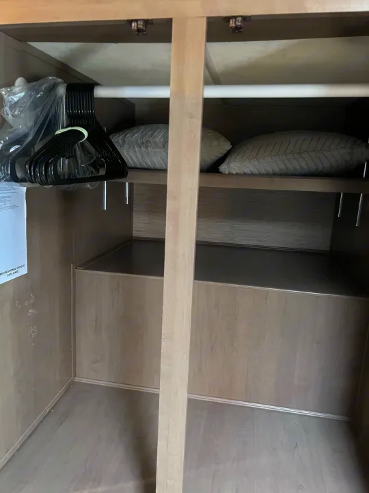 Clean RV rental wardrobe with black hangers on a rod, two pillows, and lower storage. Spacious and ready.. Thor Motor Coach Four Winds 2021