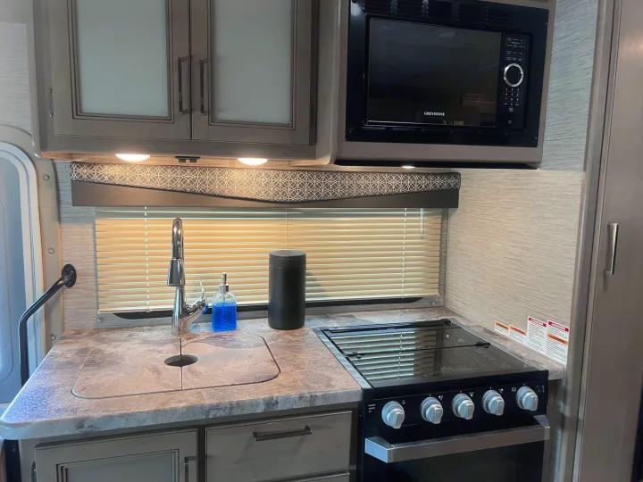 Compact rv rental kitchen with sink, stove, microwave, modern cabinets, and warm under-cabinet lighting.. Thor Motor Coach Four Winds 2021
