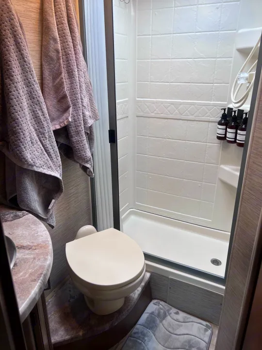 Clean RV rental bathroom with a compact shower, toilet, and vanity. Notice the hanging towels and convenient pump bottles.. Thor Motor Coach Four Winds 2021