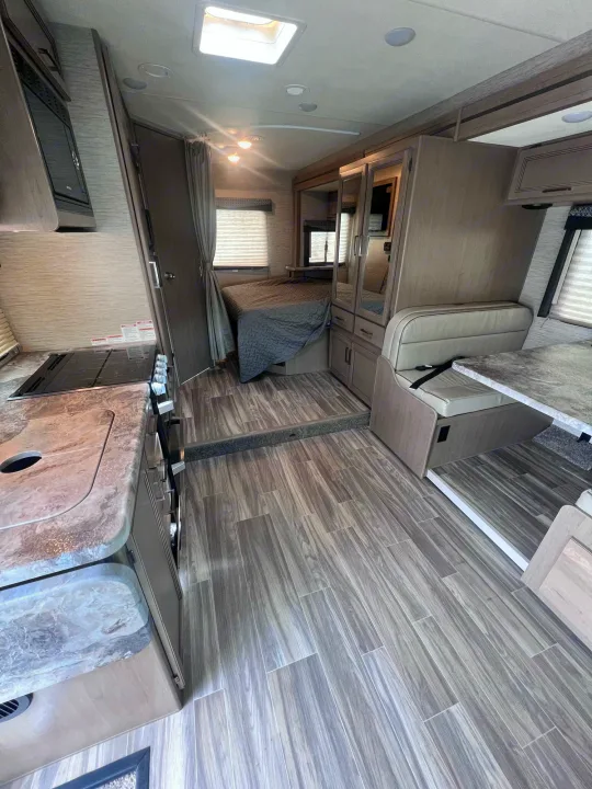 RV rental interior with a functional kitchen, elevated bedroom, and dinette area, featuring modern wood-look flooring.. Thor Motor Coach Four Winds 2021