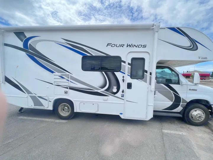 White Four Winds RV rental parked under cloudy sky, featuring blue and black graphics.. Thor Motor Coach Four Winds 2021