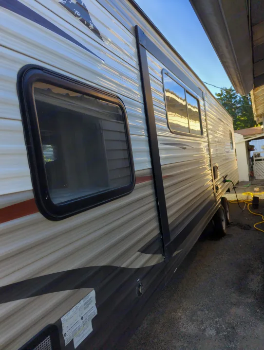 Side view of an RV rental, showing its striped exterior, windows, and utility hookups in a bright outdoor setting.. Forest River Cherokee Grey Wolf 2015