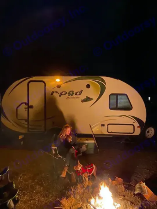 A woman and dog by a campfire, next to an R-Pod travel trailer RV rental, enjoying a night outdoors.. R-Pod Hood River Edition 2015