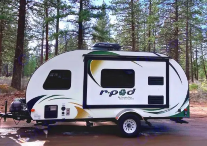 An R-Pod rv rental, a compact white travel trailer, parked among tall pines. Perfect for your next outdoor adventure.. R-Pod Hood River Edition 2015