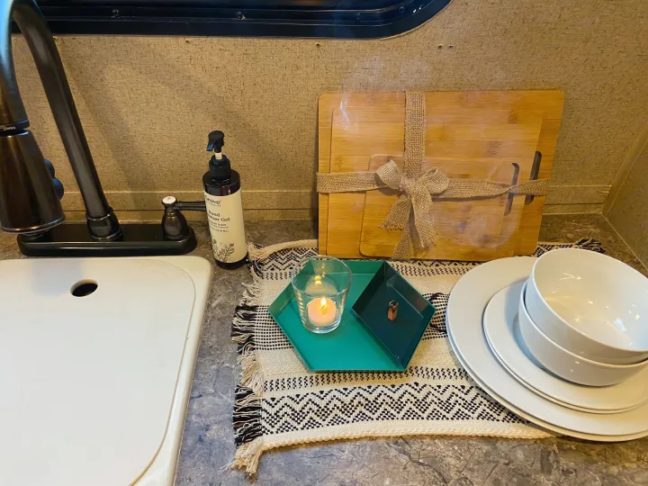 Stylish RV rental kitchen setup with sink, hand sanitizer, bamboo boards, dinnerware, and cozy candle decor.. R-Pod Hood River Edition 2015