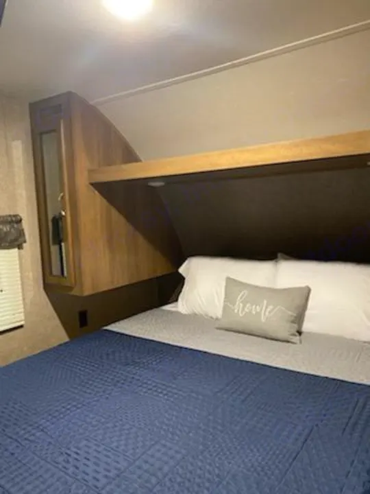 Inside an RV rental: a cozy bedroom with a blue quilted bed, white pillows, overhead storage, and light wood cabinetry.. Forest River Coachmen Catalina SBX 2017