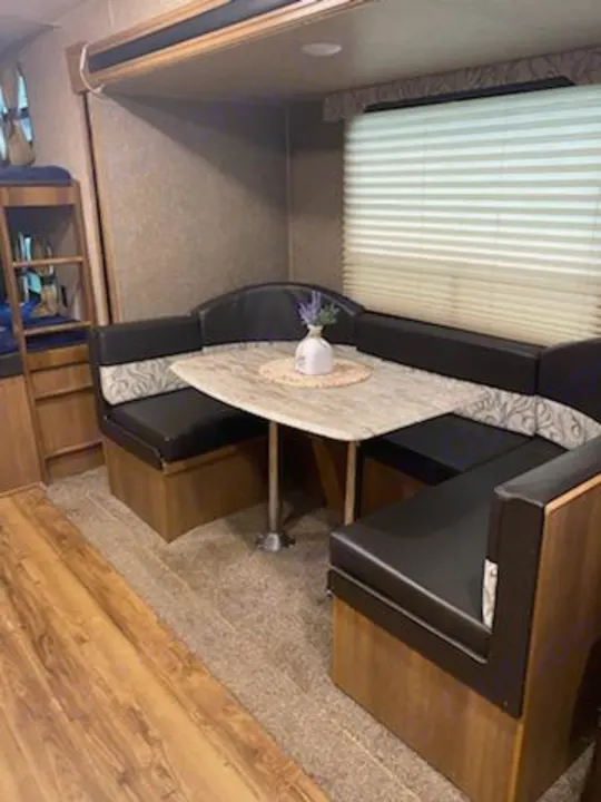 This RV rental interior features a cozy U-shaped dinette with black seating, a light table, window blinds, and mixed flooring.. Forest River Coachmen Catalina SBX 2017