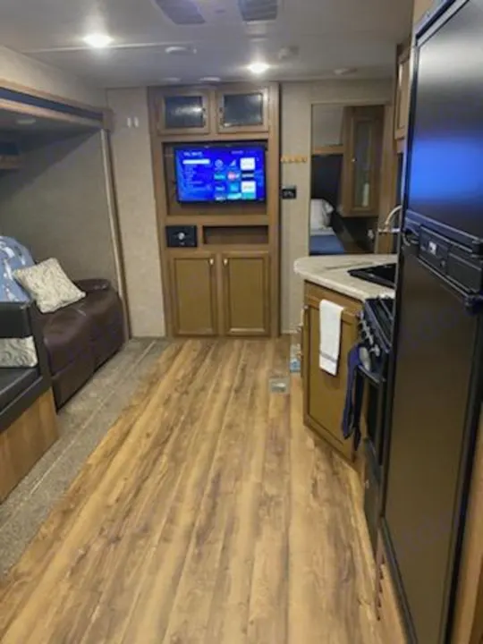 Spacious RV rental interior featuring wood flooring, an entertainment center with TV, and a full kitchen. Perfect for adventures!. Forest River Coachmen Catalina SBX 2017