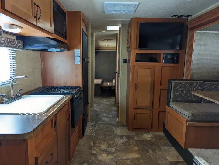 Spacious rv rental interior featuring a full kitchen with stove, microwave, and sink, plus a living area with TV and dining booth.. Forest River Cherokee Grey Wolf 2015