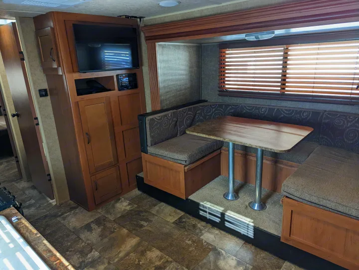 RV rental: View of a U-shaped dinette with patterned cushions, table, and entertainment center with TV. Wood cabinetry.. Forest River Cherokee Grey Wolf 2015