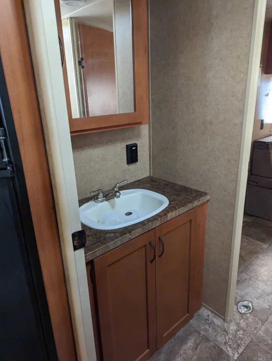 Inside an RV rental: a compact bathroom featuring a vanity with sink, mirror, and under-sink cabinet storage.. Forest River Cherokee Grey Wolf 2015
