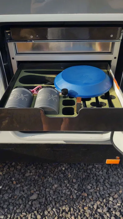 An RV rental's organized pull-out kitchen, featuring a blue plate, two gray mugs, and utensils stored neatly in custom foam.. TetonX Porter 2022
