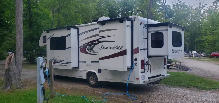 This Sunseeker RV rental is fully set up at a wooded campsite with slide-outs extended and hookups connected.. Forest River Sunseeker 2016