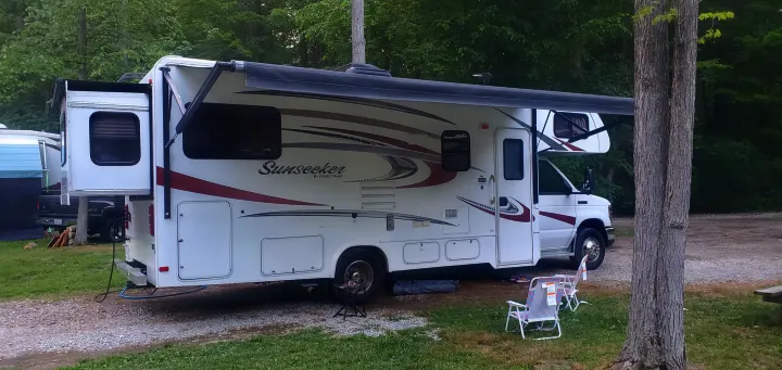 White Sunseeker RV rental motorhome at a peaceful campsite, with its slide-out extended and awning open for leisure.. Forest River Sunseeker 2016